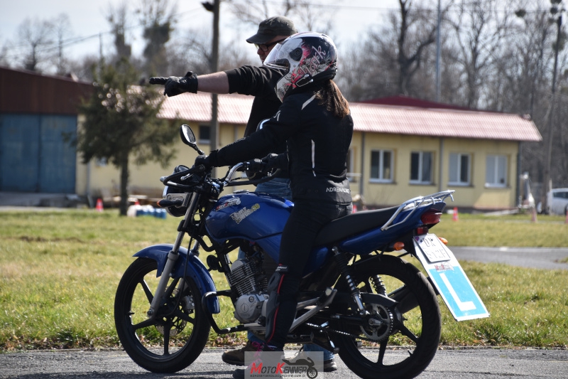 Instruktor motocyklowy demonstrujący prawidłową pozycję na motocyklu kursantce na szkoleniu kategorii A1.