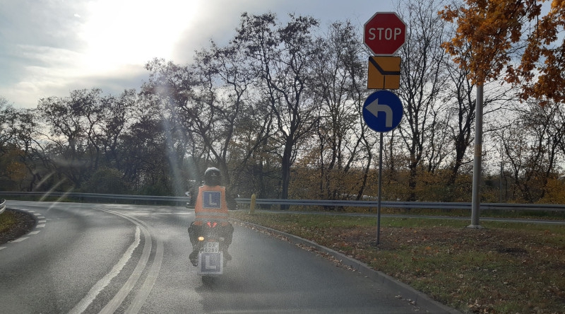 Kursant jadący na motocyklu obok znaków drogowych przed zdawaniem na prawo jazdy kategorii AM