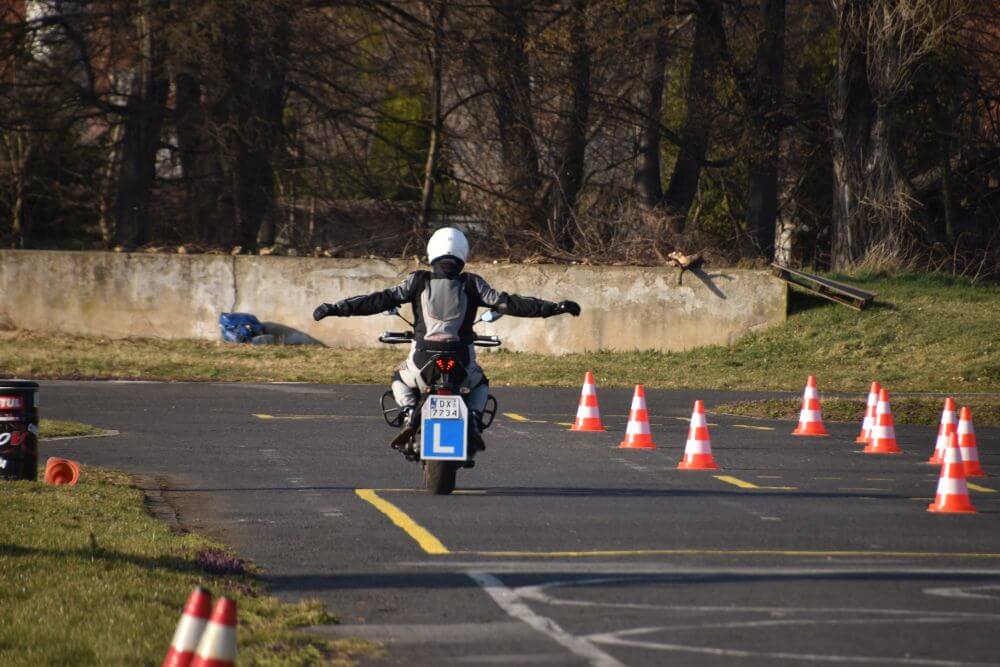 Początkujący kierowca ćwiczący równowagę na motocyklu z rozłożonymi ramionami na kursie na prawo jazdy kategorii A.
