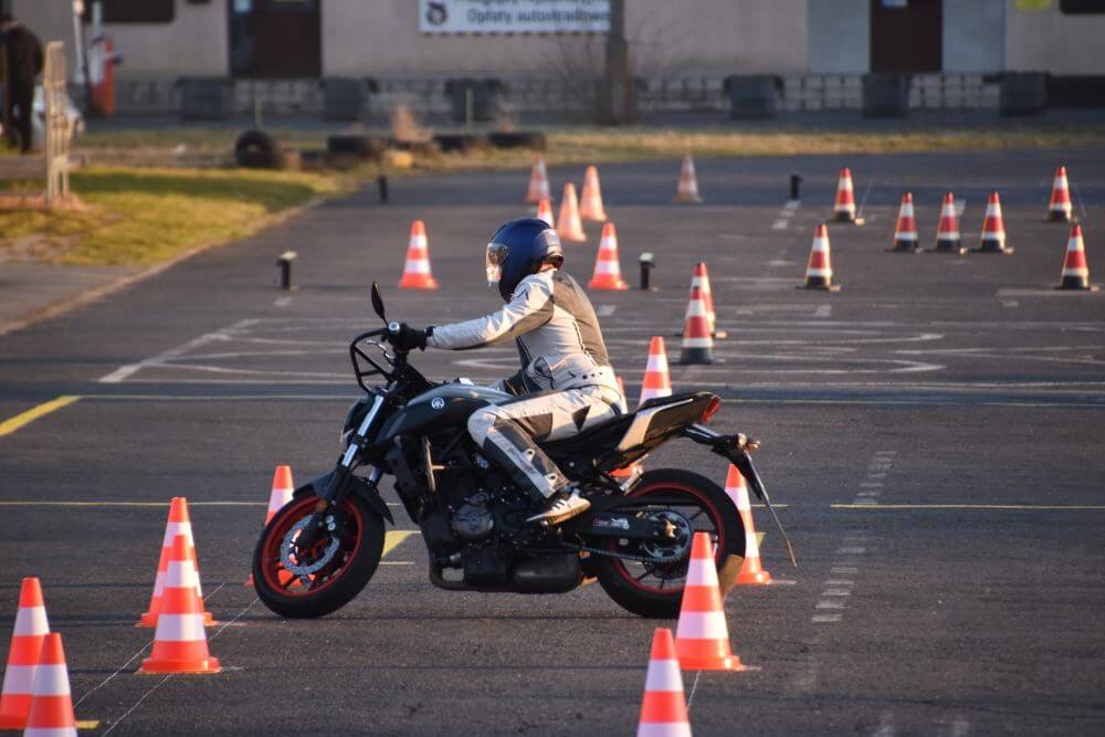 Początkujący motocyklista wykonujący slalom wokół pachołków na placu szkoleniowym na prawo jazdy kategorii A.
